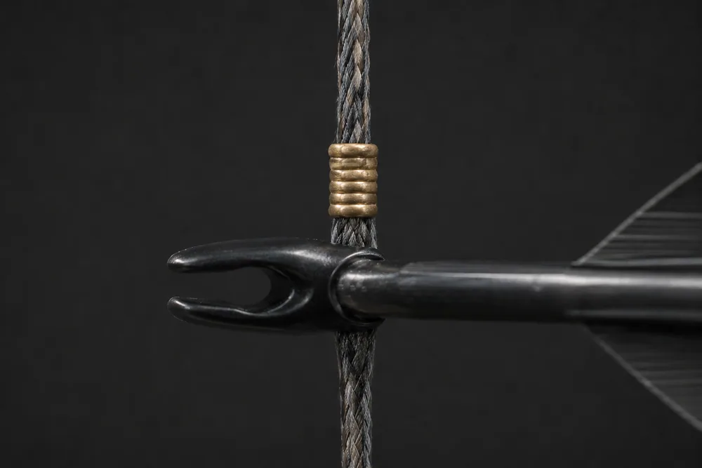 Close-up of a brass nock locator crimped on a bowstring serving with a carbon arrow nocked just beneath it.