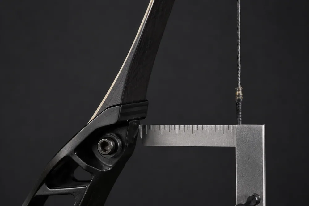 Close-up of a recurve bow lower limb at the riser with a square ruler measuring the distance to the bowstring (tiller).